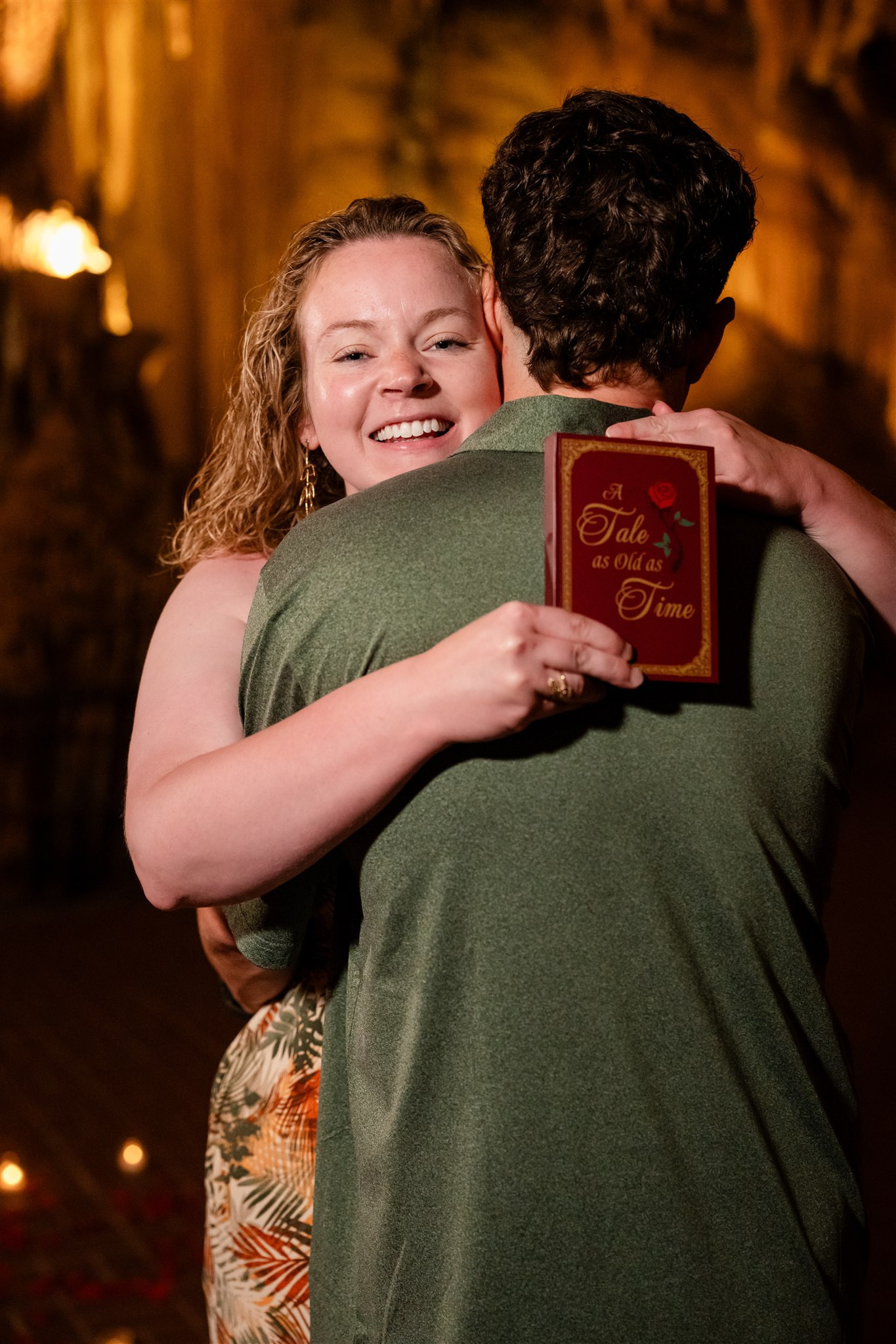 Woman hugs man, holding "A Tale as Old as Time" book. Luray Caverns proposal.