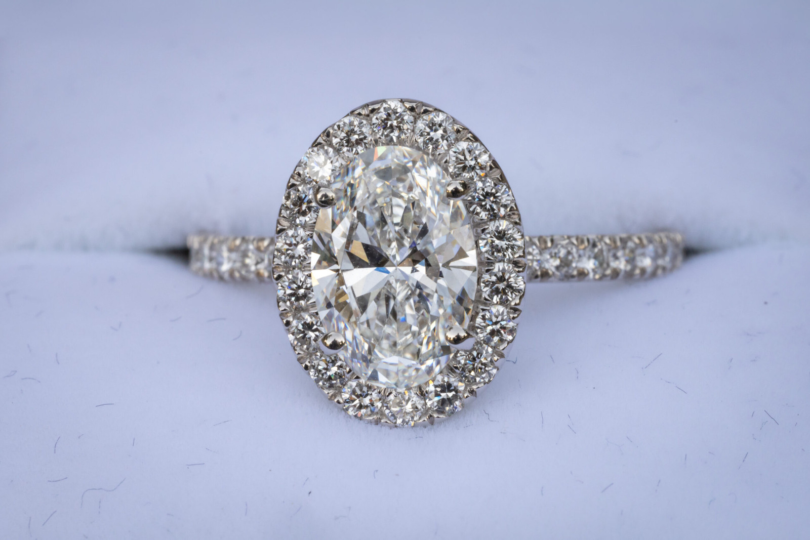 Oval diamond engagement ring with halo setting in a blue box.