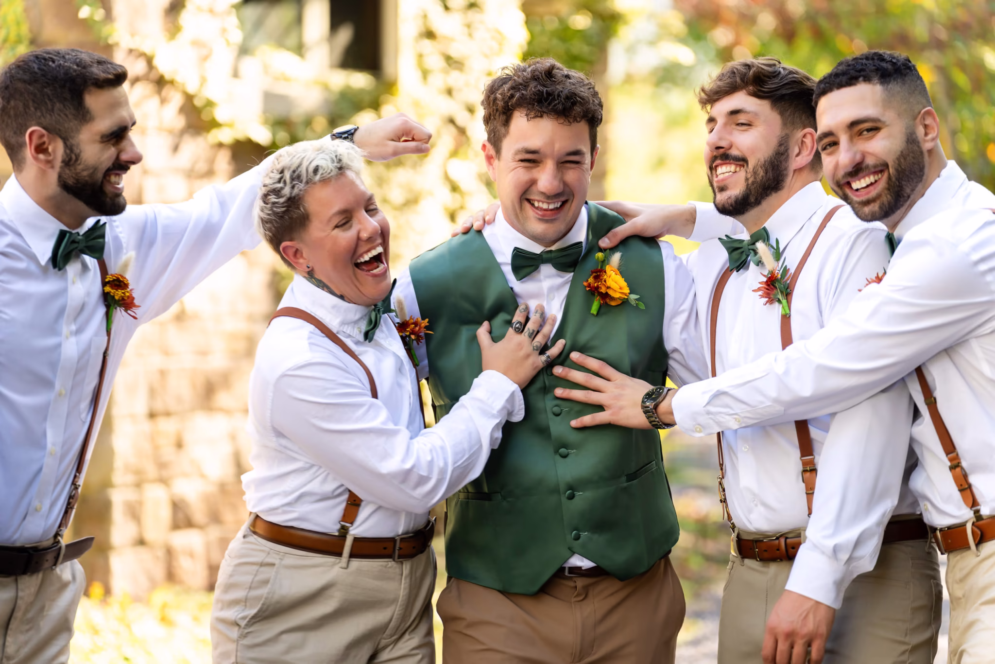 Groom laughs with groomsmen and bridesman in suspenders and bowties.