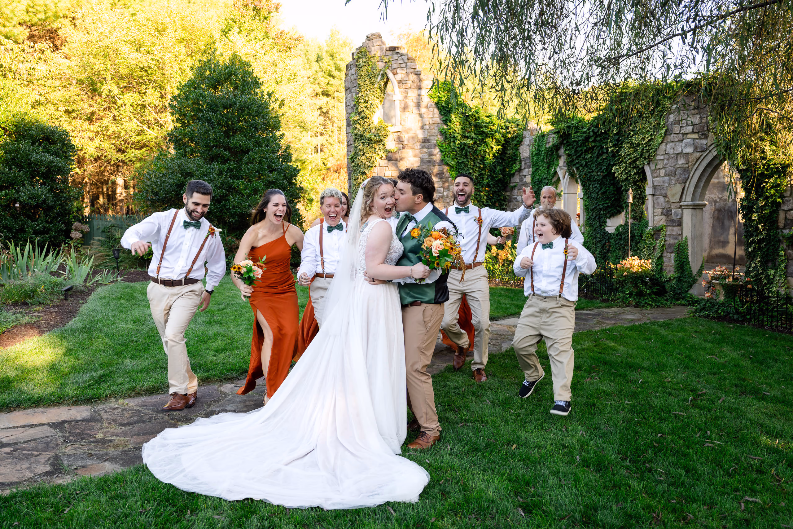 Bride and groom kissing with wedding party cheering outdoors