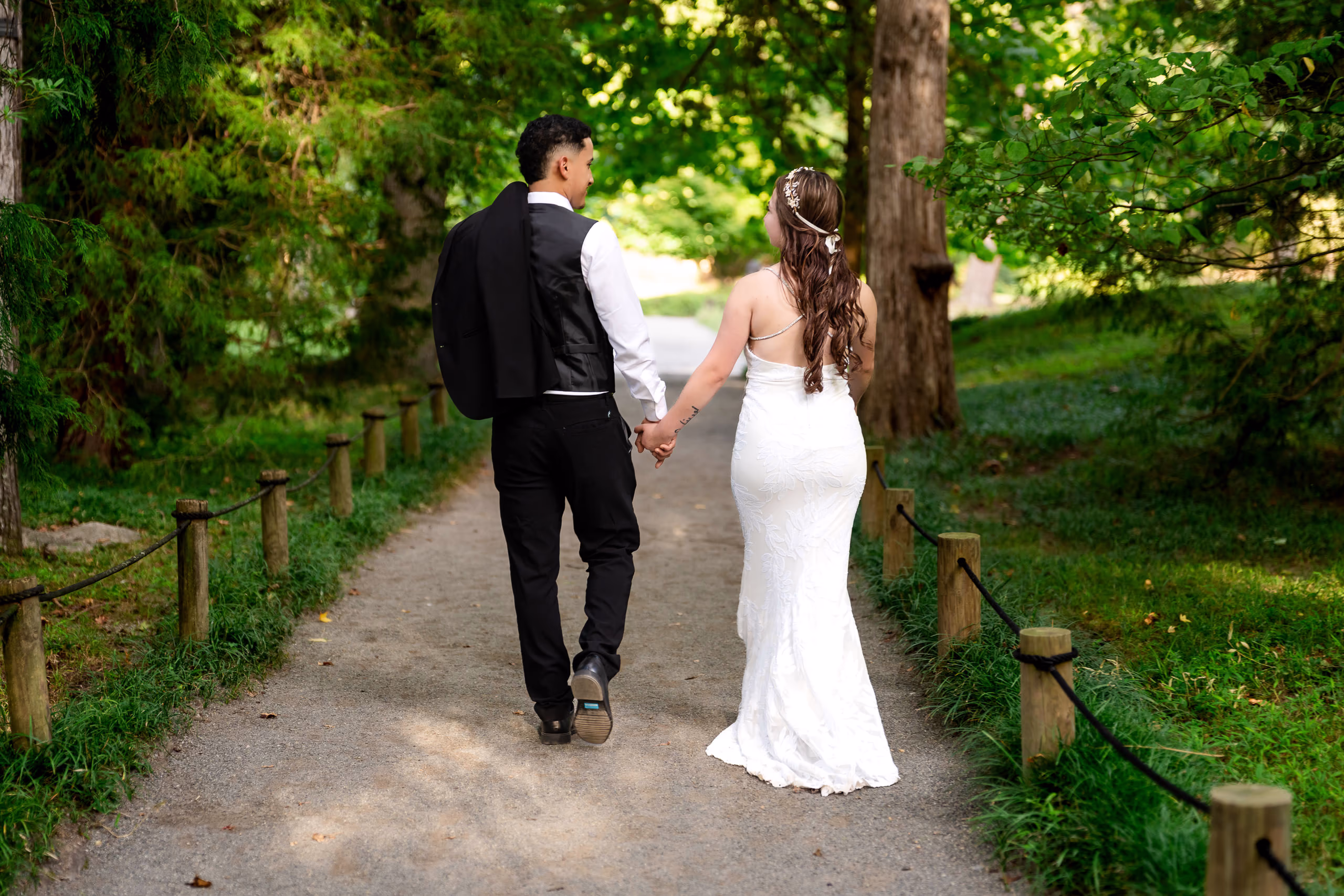 Newlyweds walk hand-in-hand along a tree-lined path.