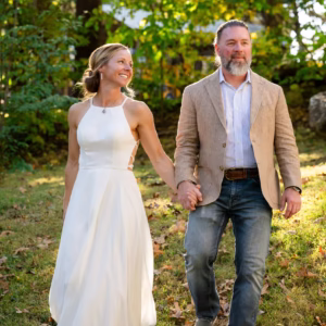 Couple holding hands in a garden, wearing wedding attire.