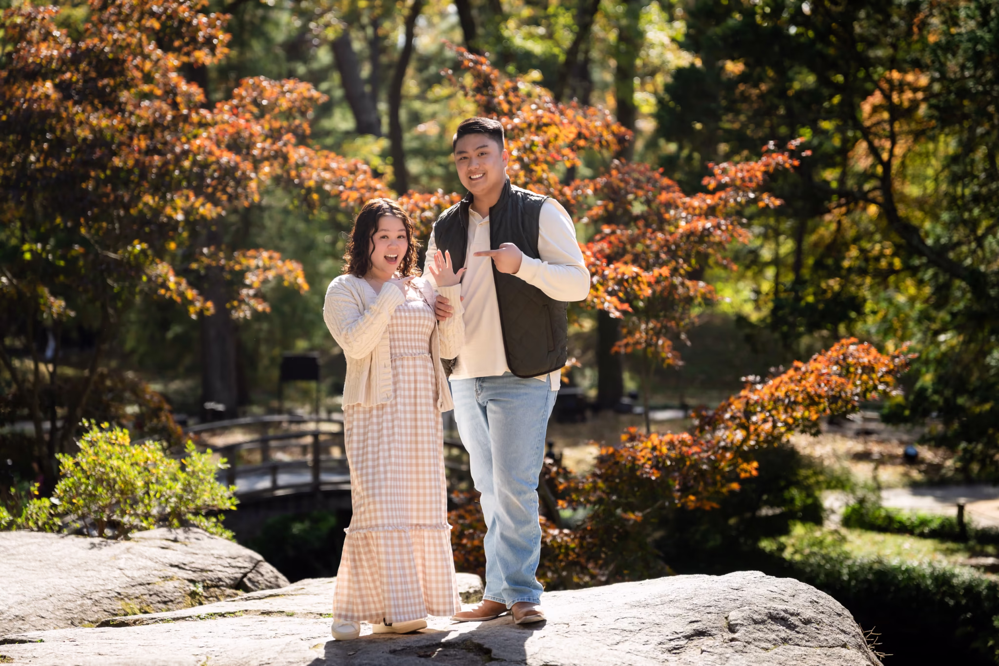 Couple poses outdoors with fall foliage in background.