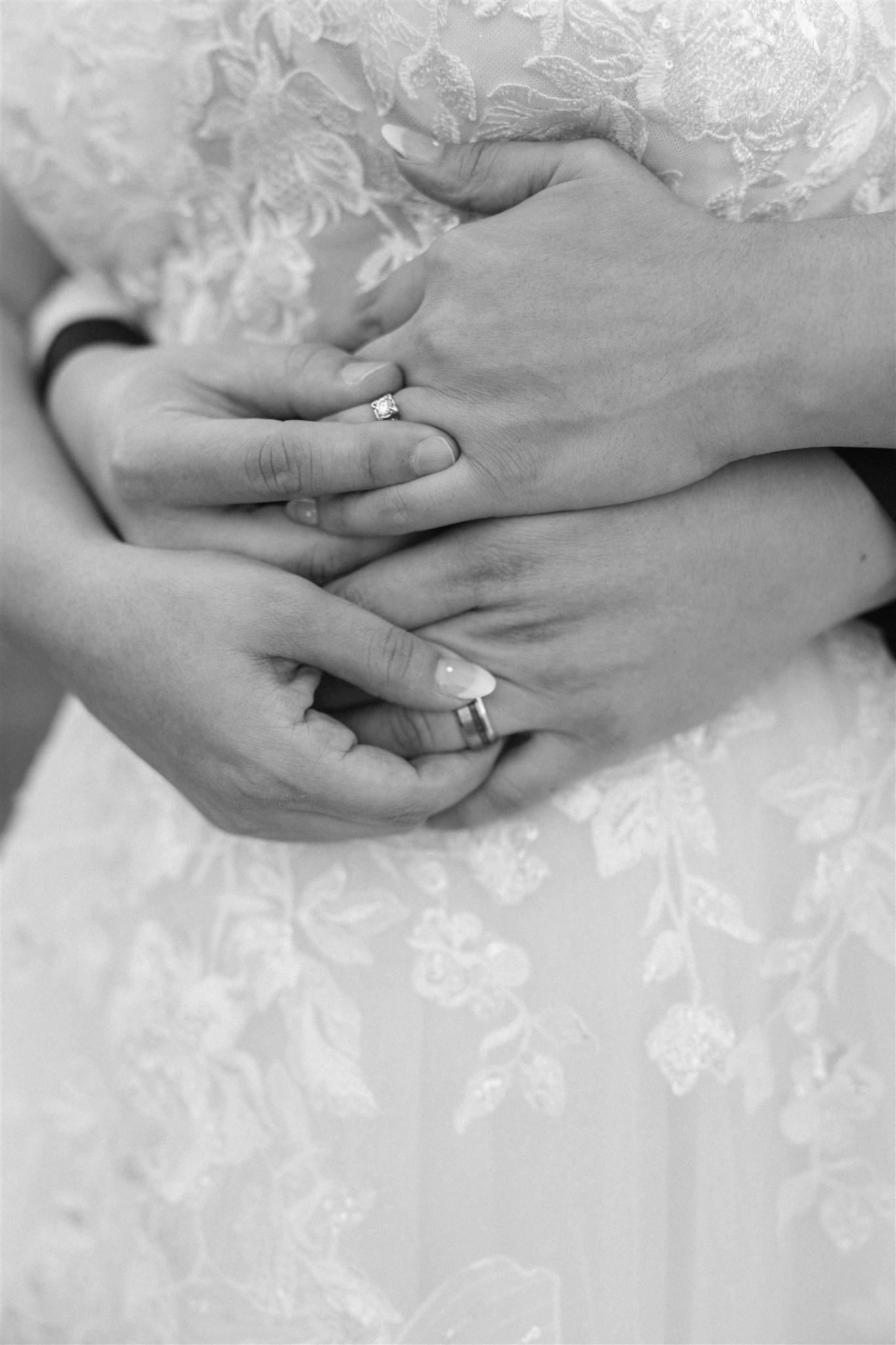 Hands with wedding rings embrace over a lace wedding dress