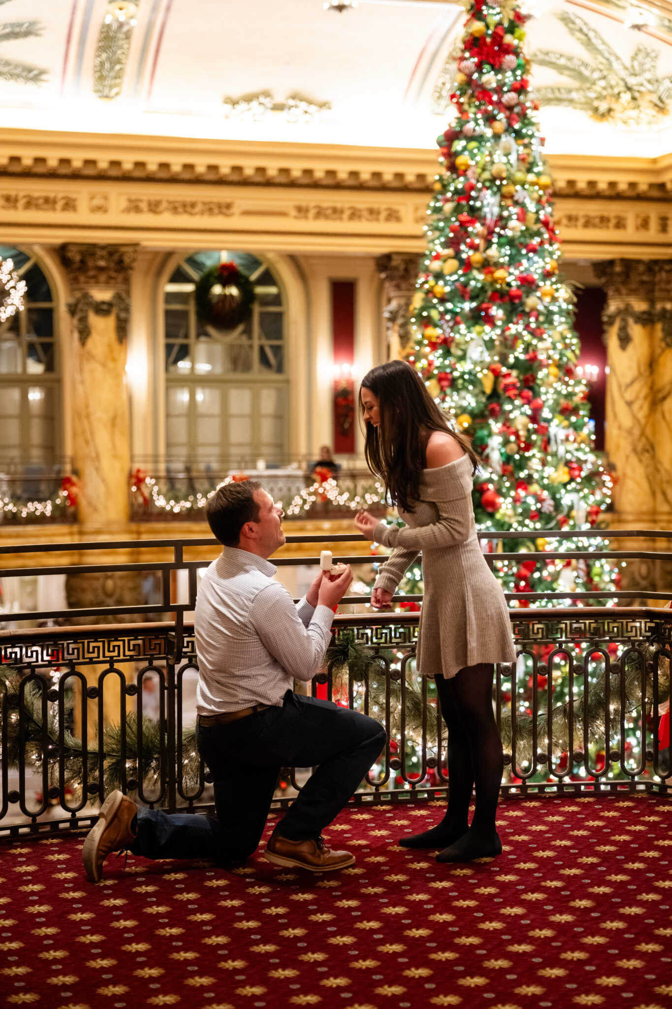 Man proposes to woman in front of Christmas tree.