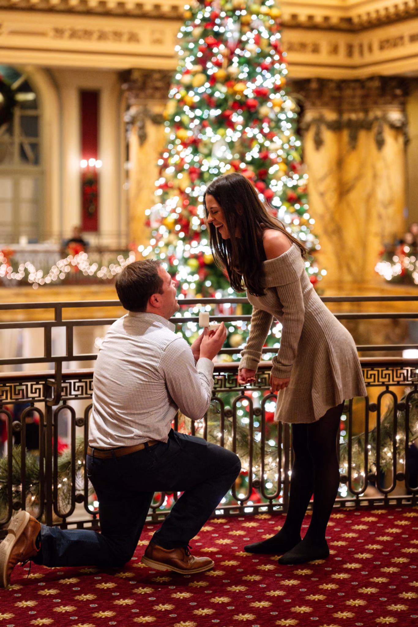 Man proposing to woman at Christmas with tree in background.